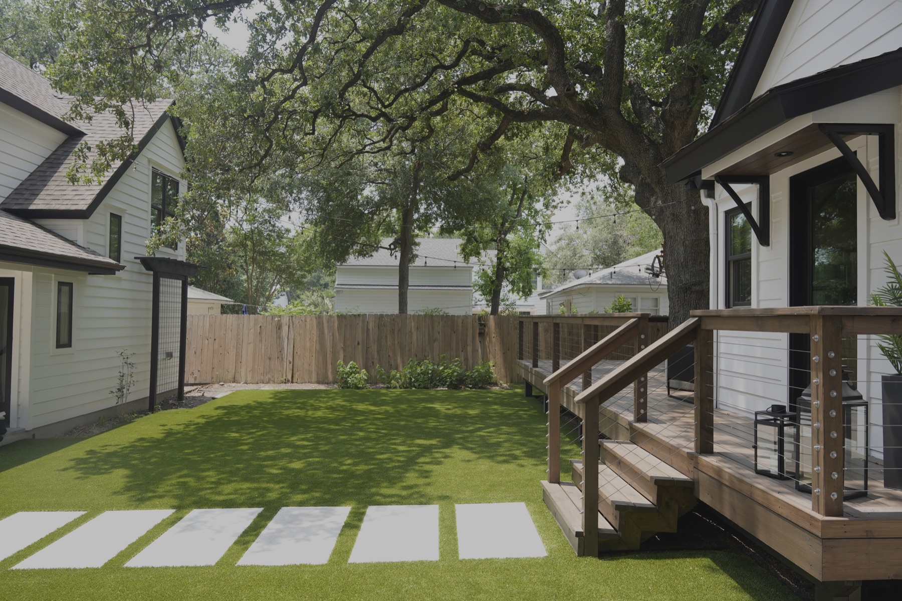 Backyard turf installation beside a cedar deck under mature shade trees