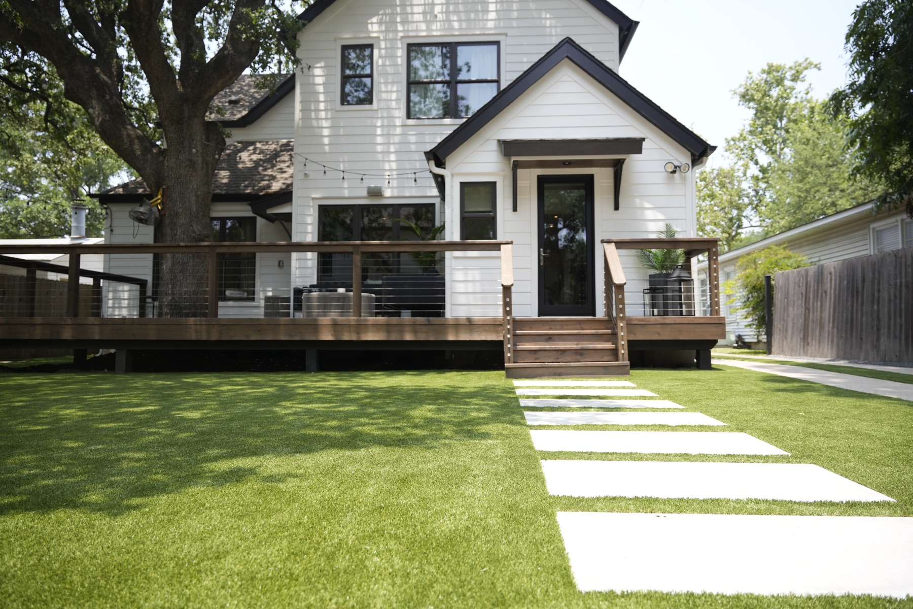Artificial turf front lawn with concrete paver walkway leading to a modern white farmhouse