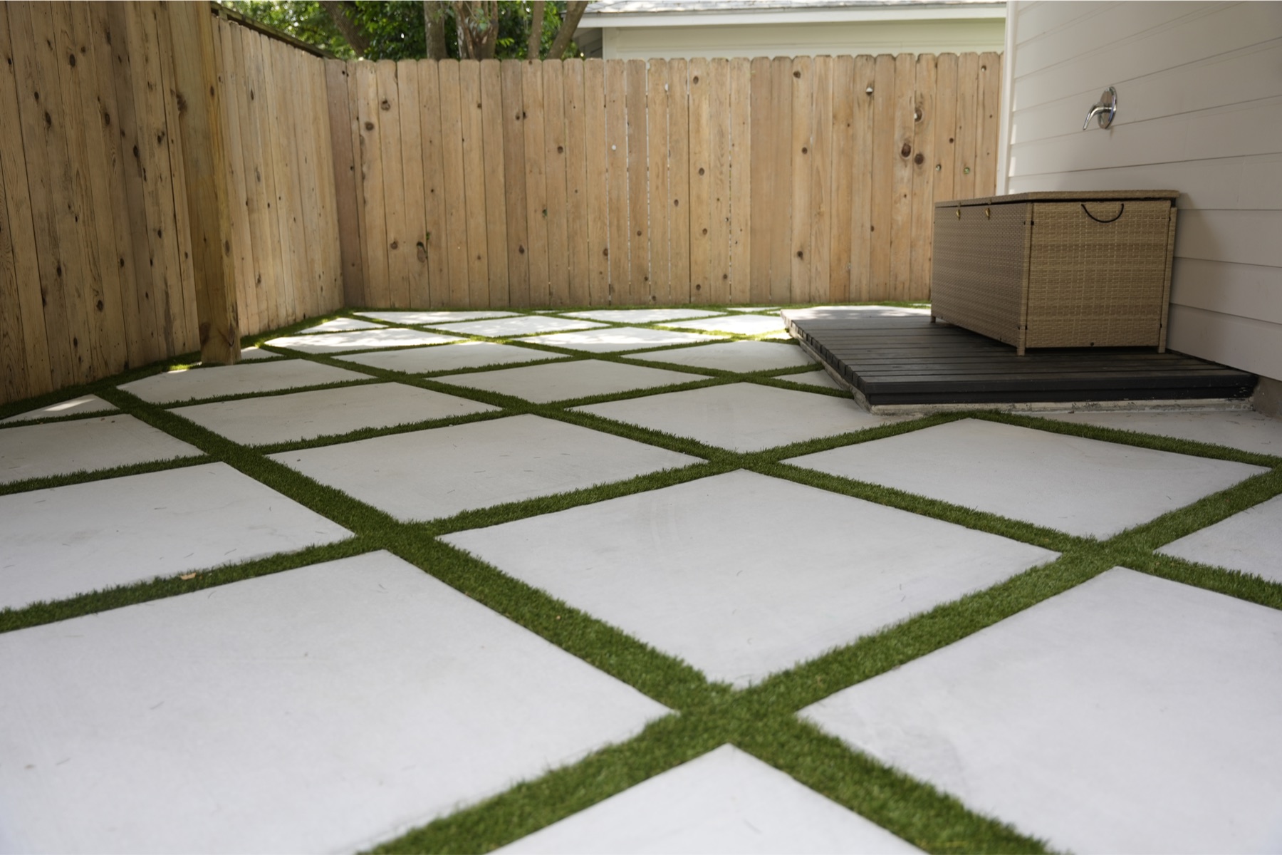 Large-format concrete pavers with turf ribbons between them in a fenced side yard