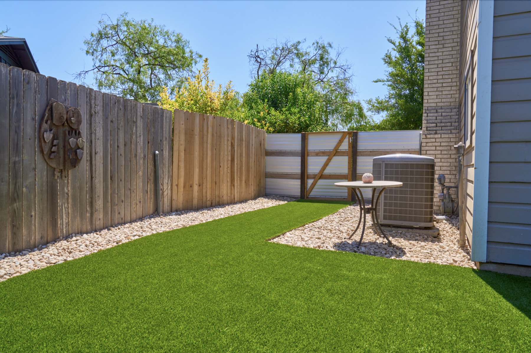 Narrow side-yard turf strip bordered by river rock and a wood privacy fence